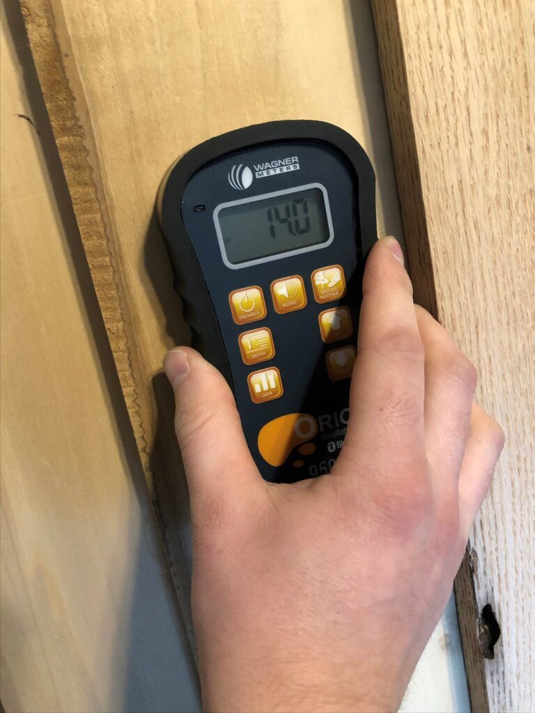 Hand-held moisture meter pressed against a wall to check for hidden dampness